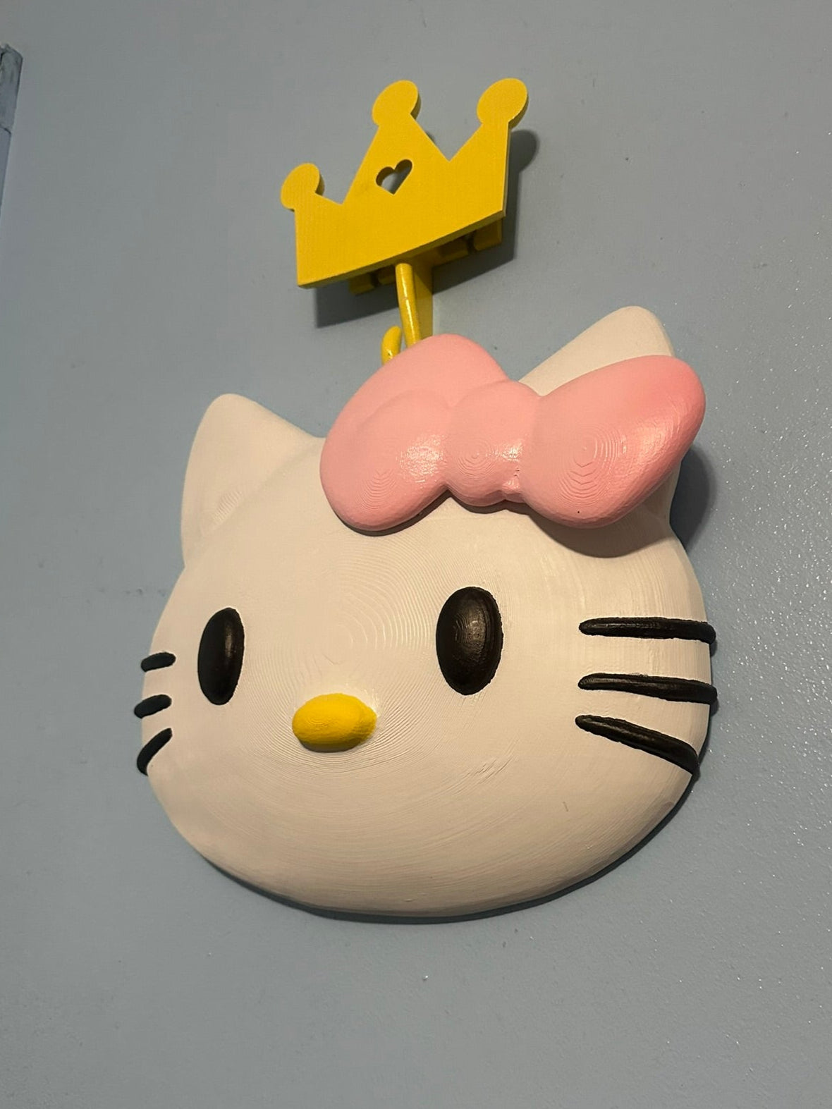 Hello Kitty-shaped object with a pink bow and yellow crown on a gray background